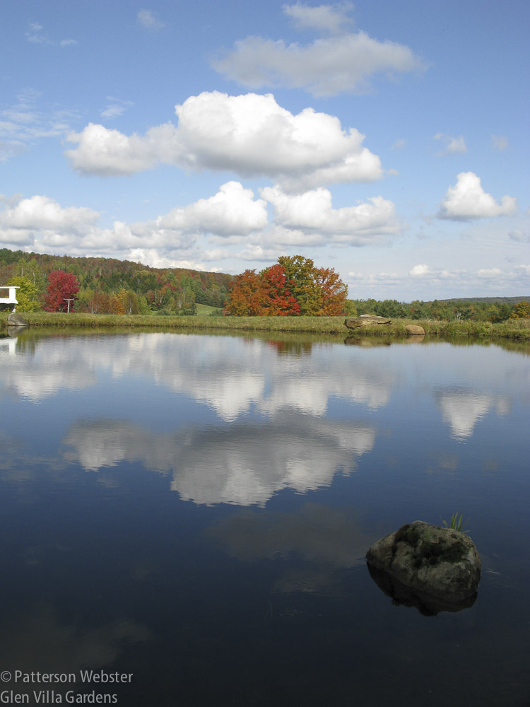 Blue sky, puffy white clouds and autumn colour are reflected in the Skating Pond at Glen Villa.