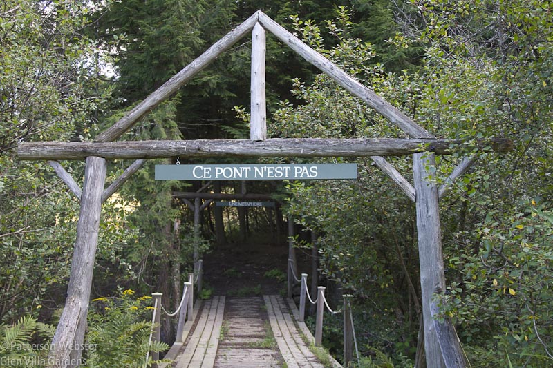 The first sign reads 'This bridge is not". On the other side of the bridge a second sign read "a metaphor." From the other side of the bridge, the text is in English. 