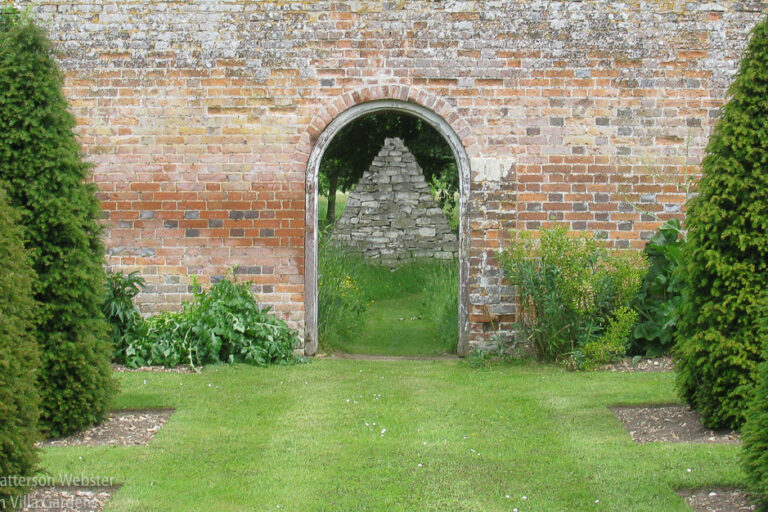 A door in a brick wall at The Grove, the garden of the late David Hicks, frames the view of a stone construction beyond.