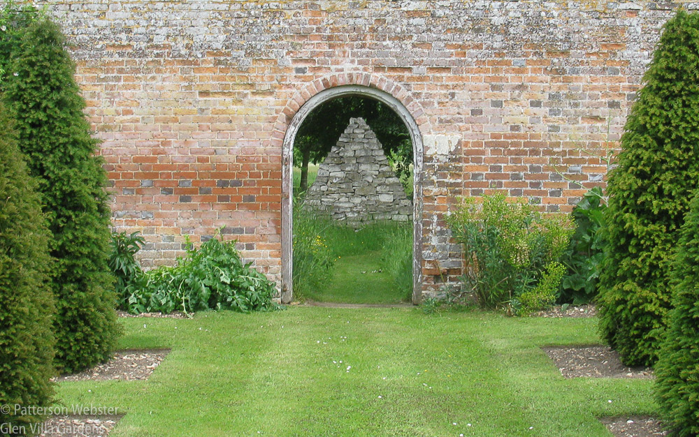 A door in a brick wall at The Grove, the garden of the late David Hicks, frames the view of a stone construction beyond.