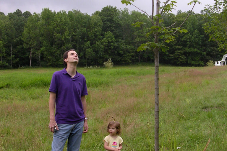 One grandchild stands next to her tree along with her father.