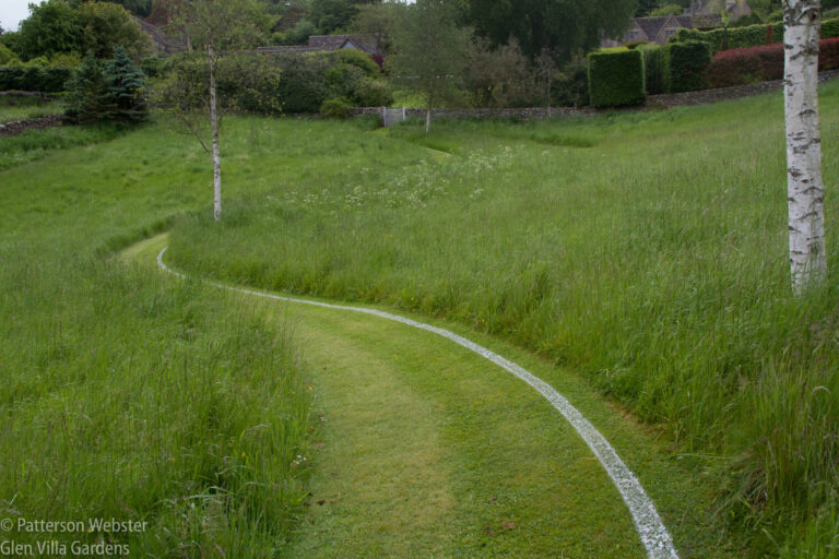 A curving parth at Througham Court leads across a field to a gate banners flying in the distance.